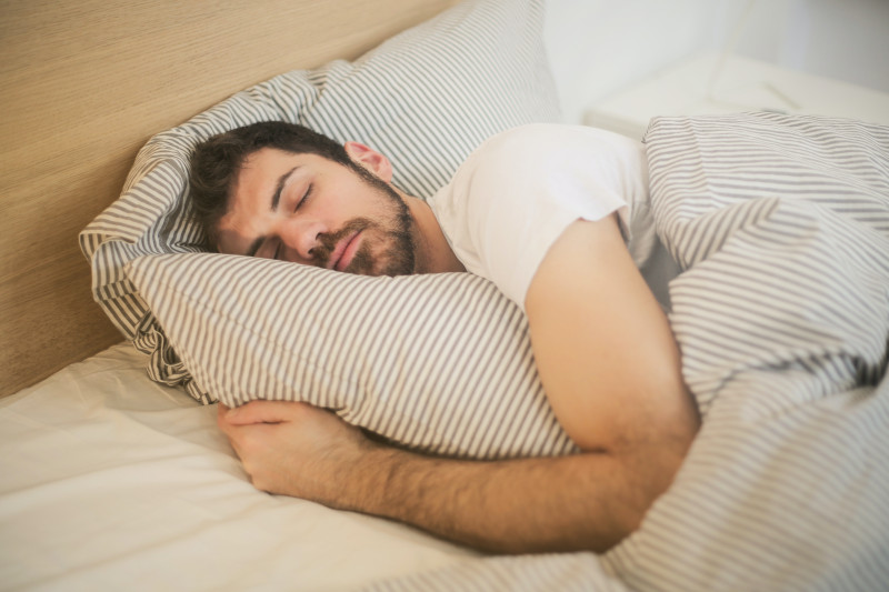 A man sleeping soundly in his bed, striped sheets pulled up around him.