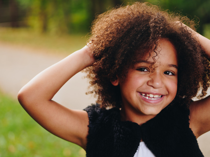 A young girl with long curly hair and a wide, toothy grin