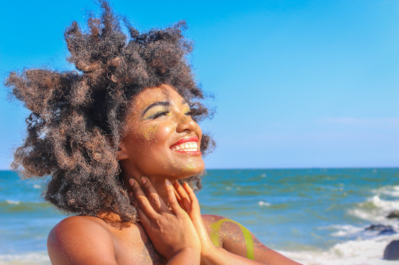 Woman smiling on a bright, cloudless day on the beach.